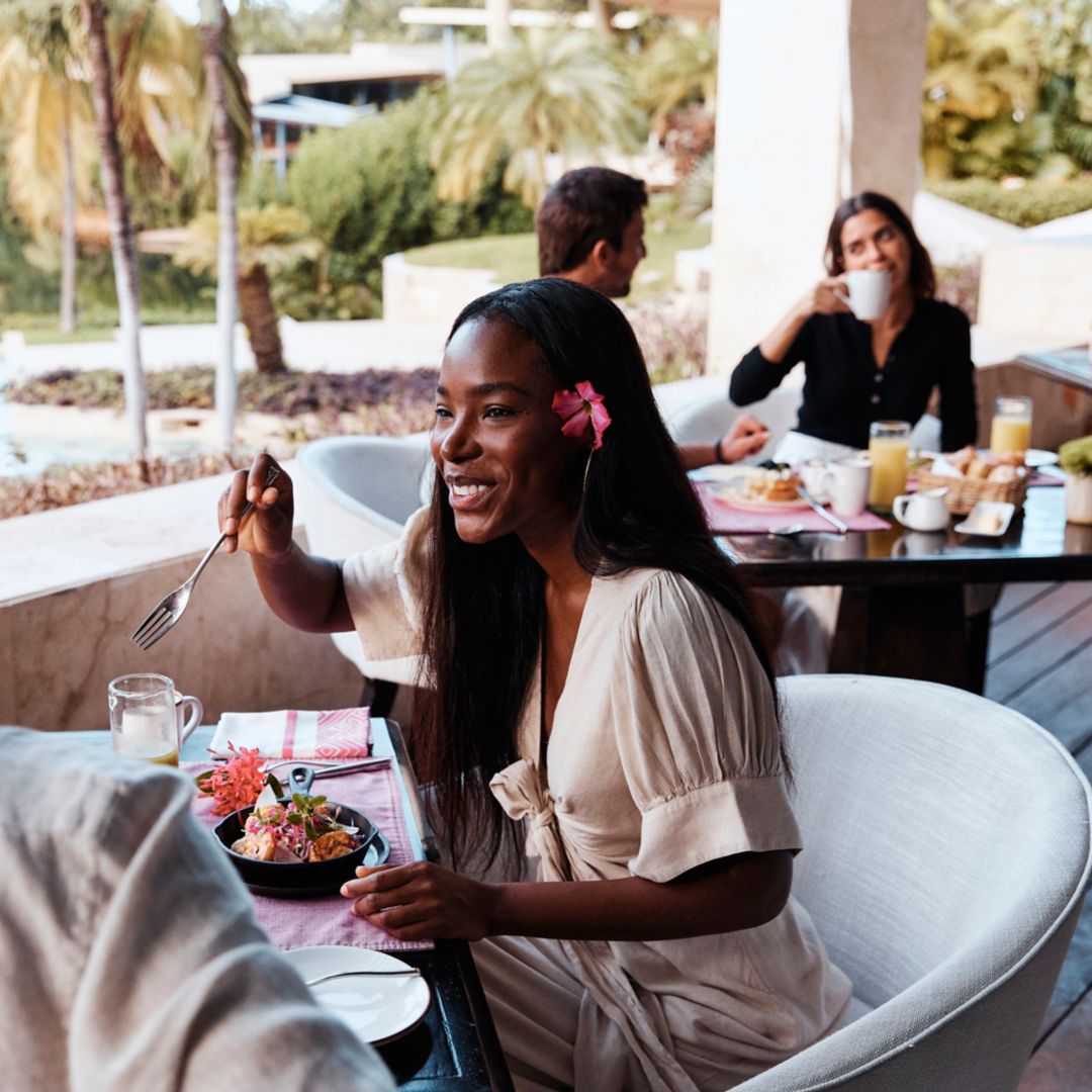 A woman enjoying a meal at an outdoor restaurant surrounded by greenery and palm trees.