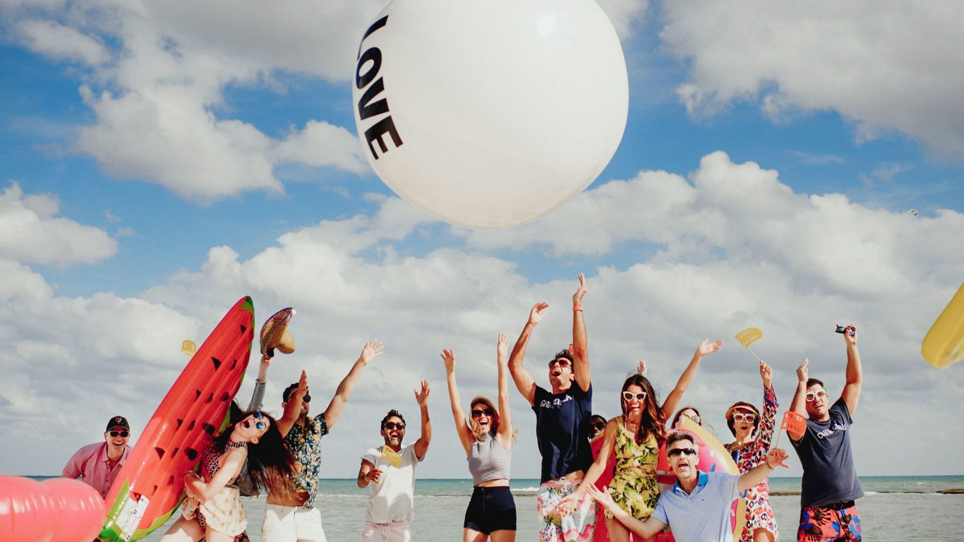two woman and a man with sunglasses laugh and drink on the beach 