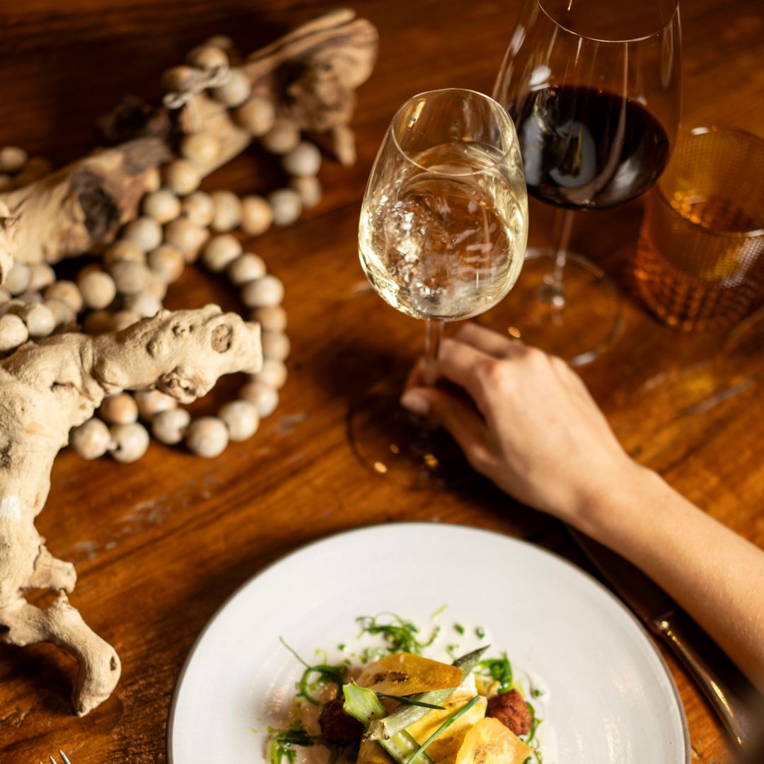 A person holding a wine glass next to a plate  of Lobster Ceviche.