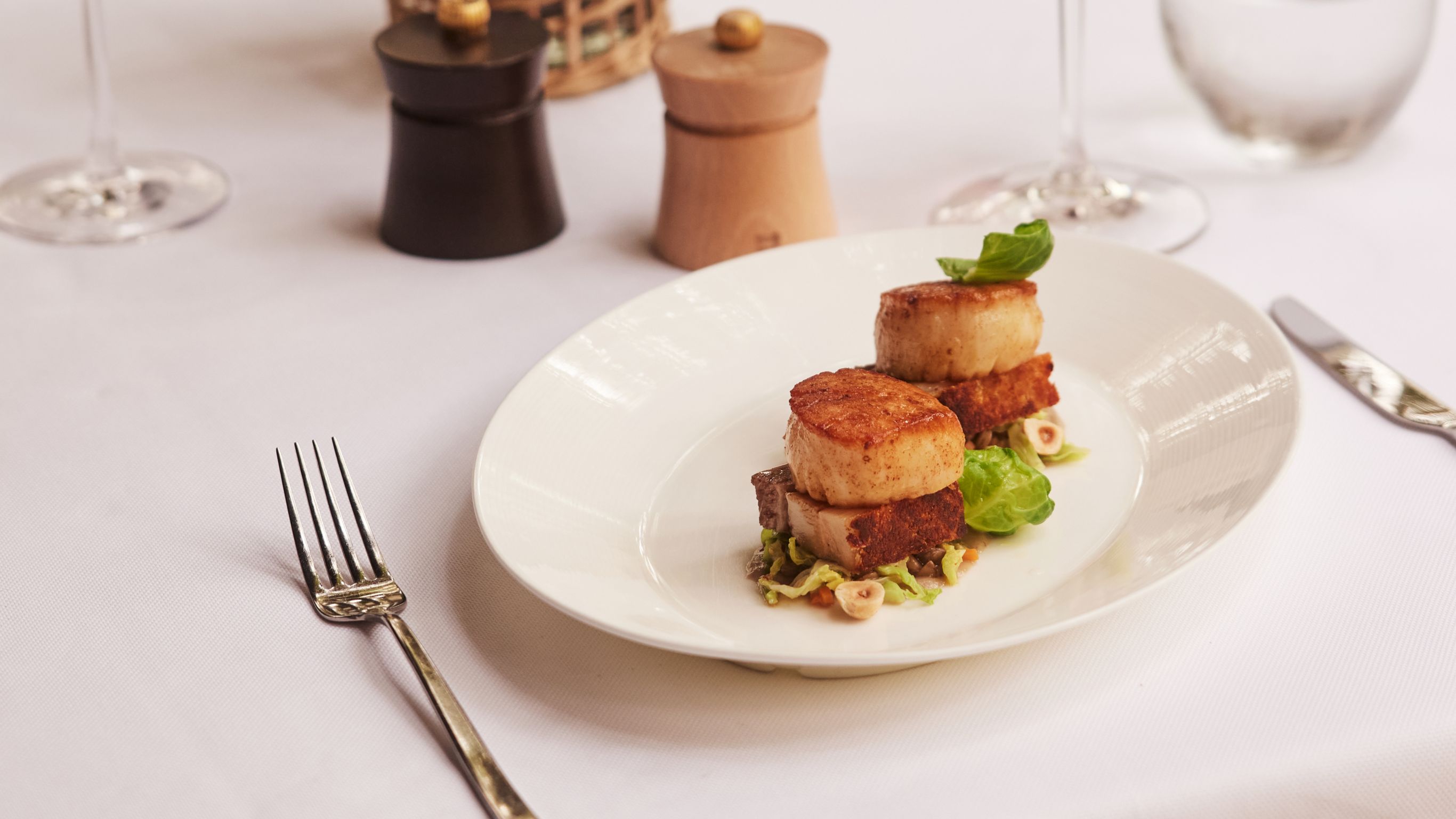 A table setting with scallops on a plate, glasses of wine, water, and a vase of flowers.