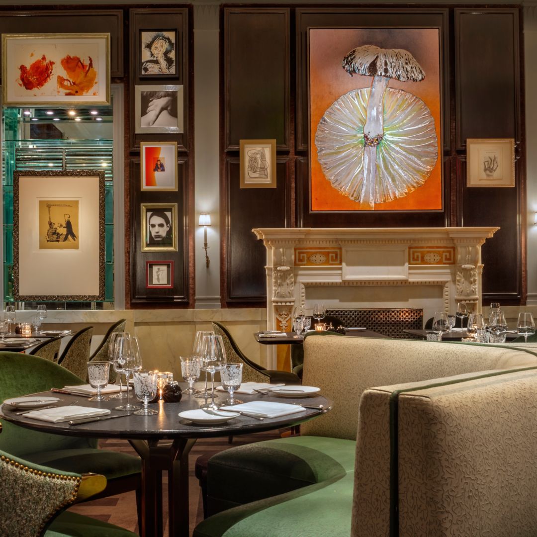 A dining area with green chairs, artwork, a fireplace, and elegantly set tables.