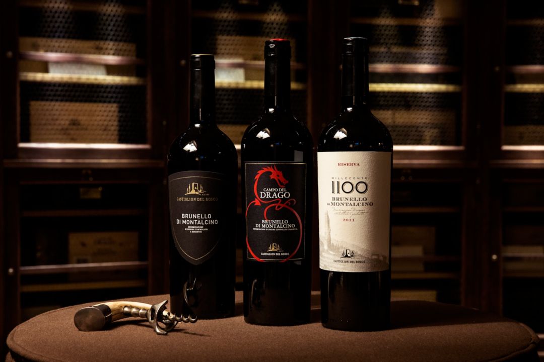 Three wine bottles labeled "Brunello di Montalcino" with a corkscrew on a table.