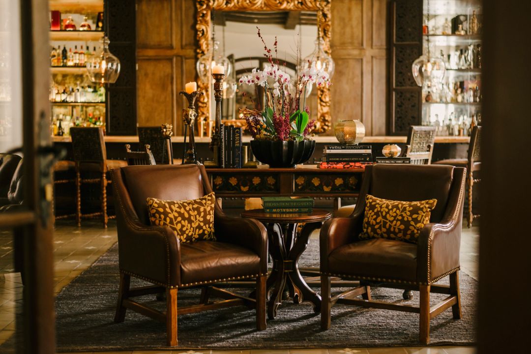 A tequila bar with leather chairs, a table with books, and a mirror in the background.