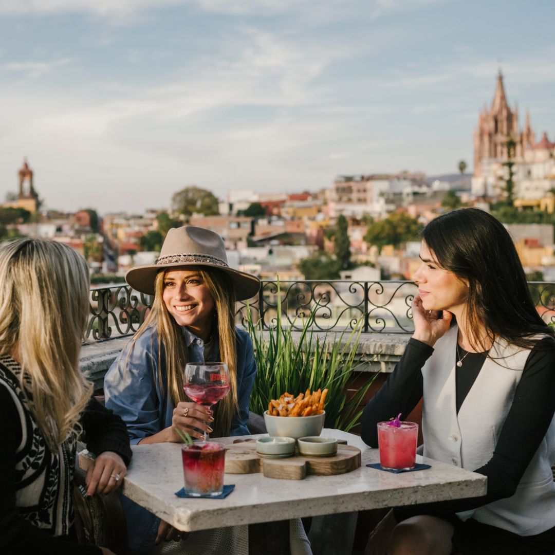 Three women enjoying drinks and appetizers at a rooftop restaurant in San Miguel de Allende.