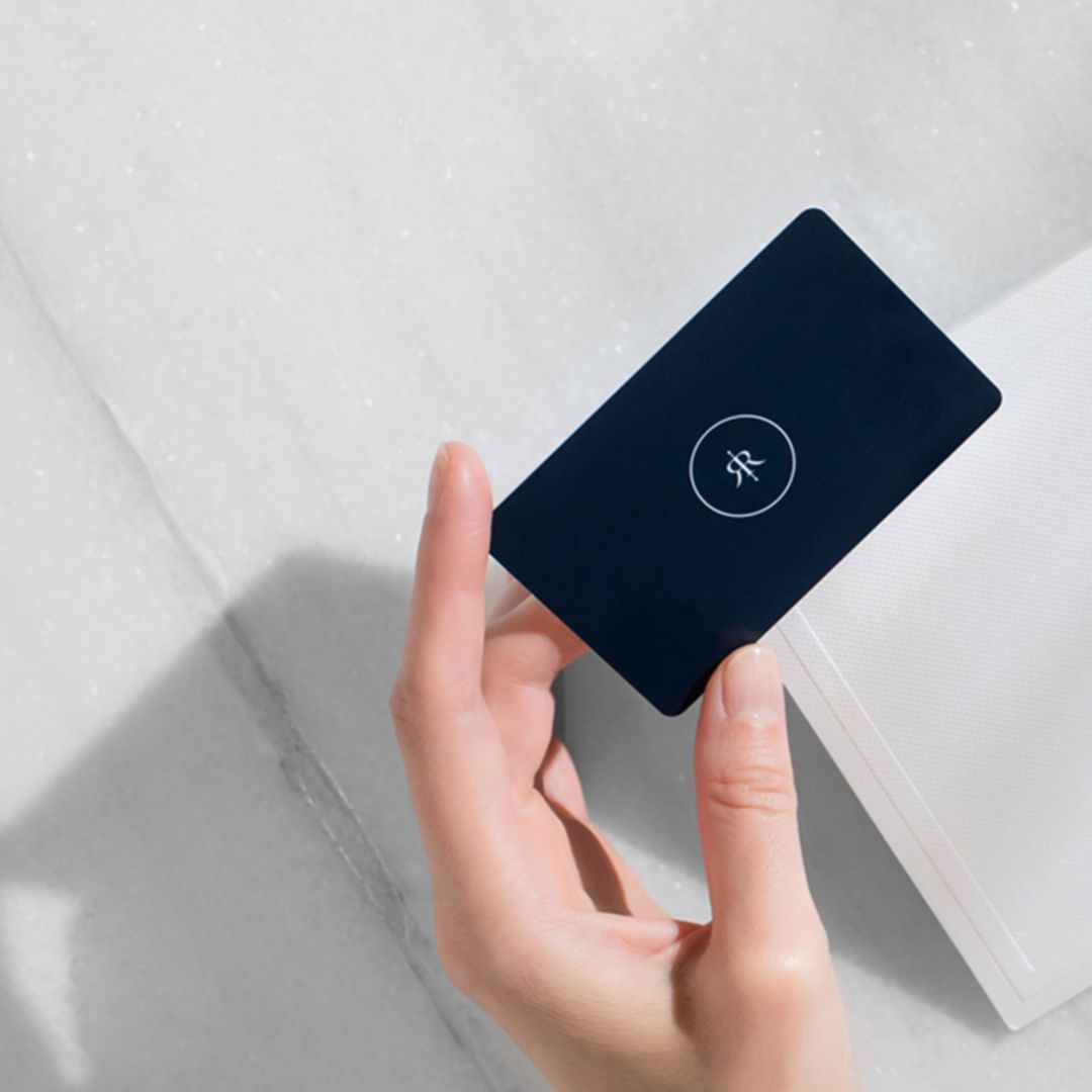 A hand holding a black hotel gift card over a white envelope on a marble surface.
