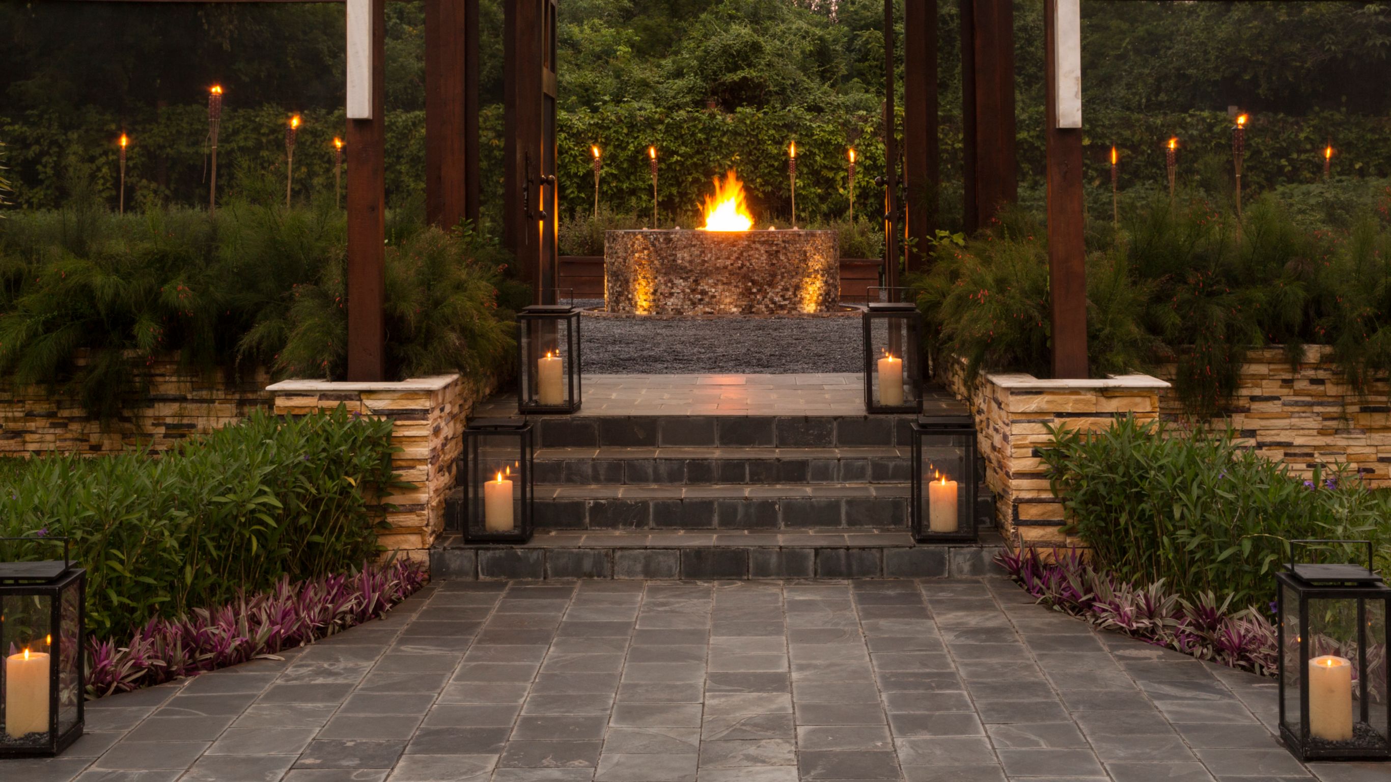 mesa longa de madeira comunitária com bancos sob árvore ceiba imponente, com lanternas redondas penduradas nos galhos, em um jardim ao pôr do sol