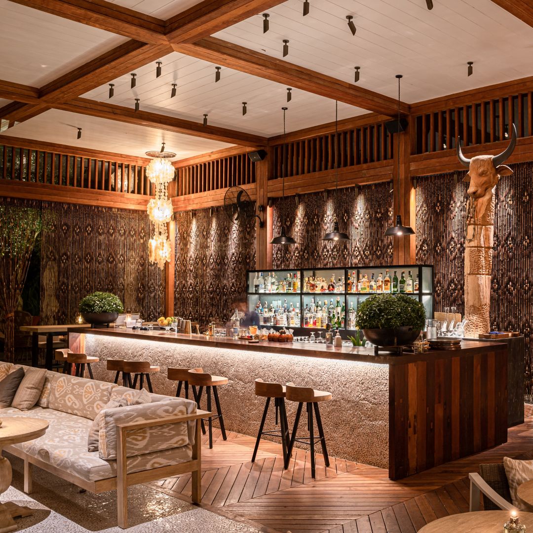A stylish bar at Rosewood Phuket, featuring wooden decor, a well-stocked bar, and comfortable seating.