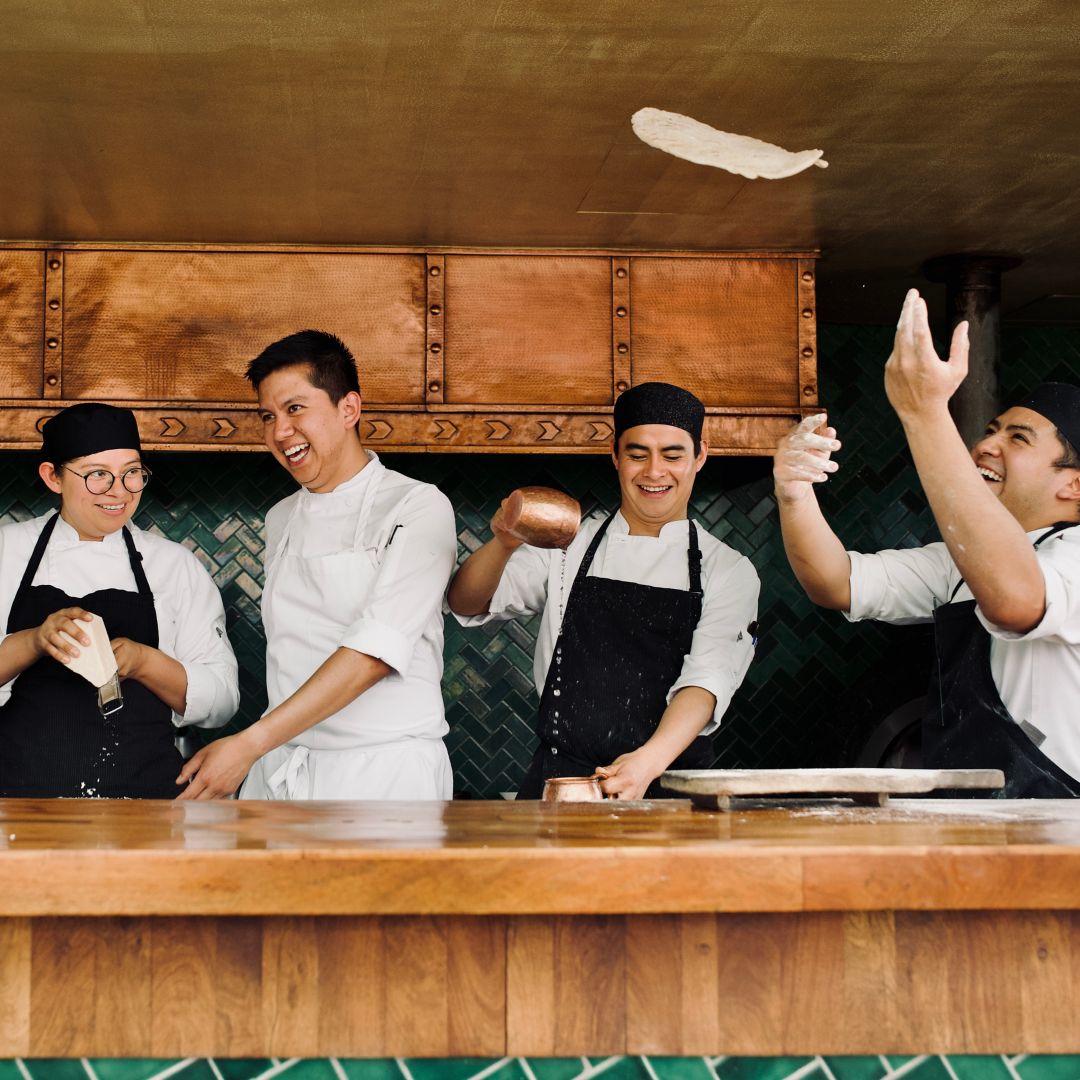 Chefs laughing and preparing food in an open  kitchen.