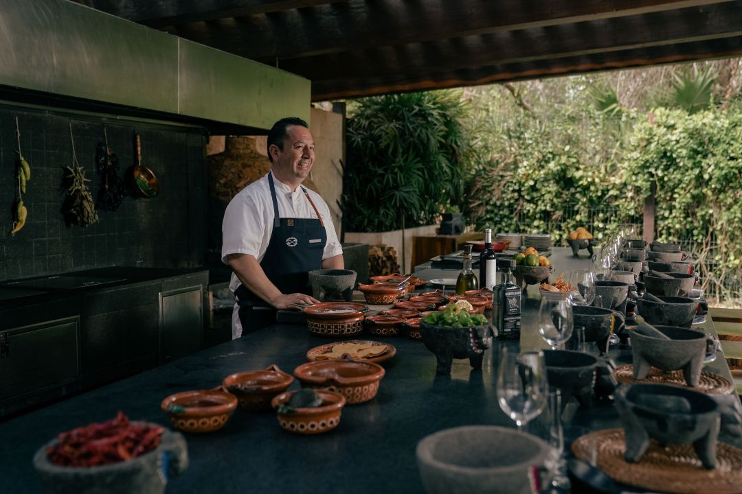 Plated trio of tacos with jalapenos and lime staged next to abottle of tequila on stone platter