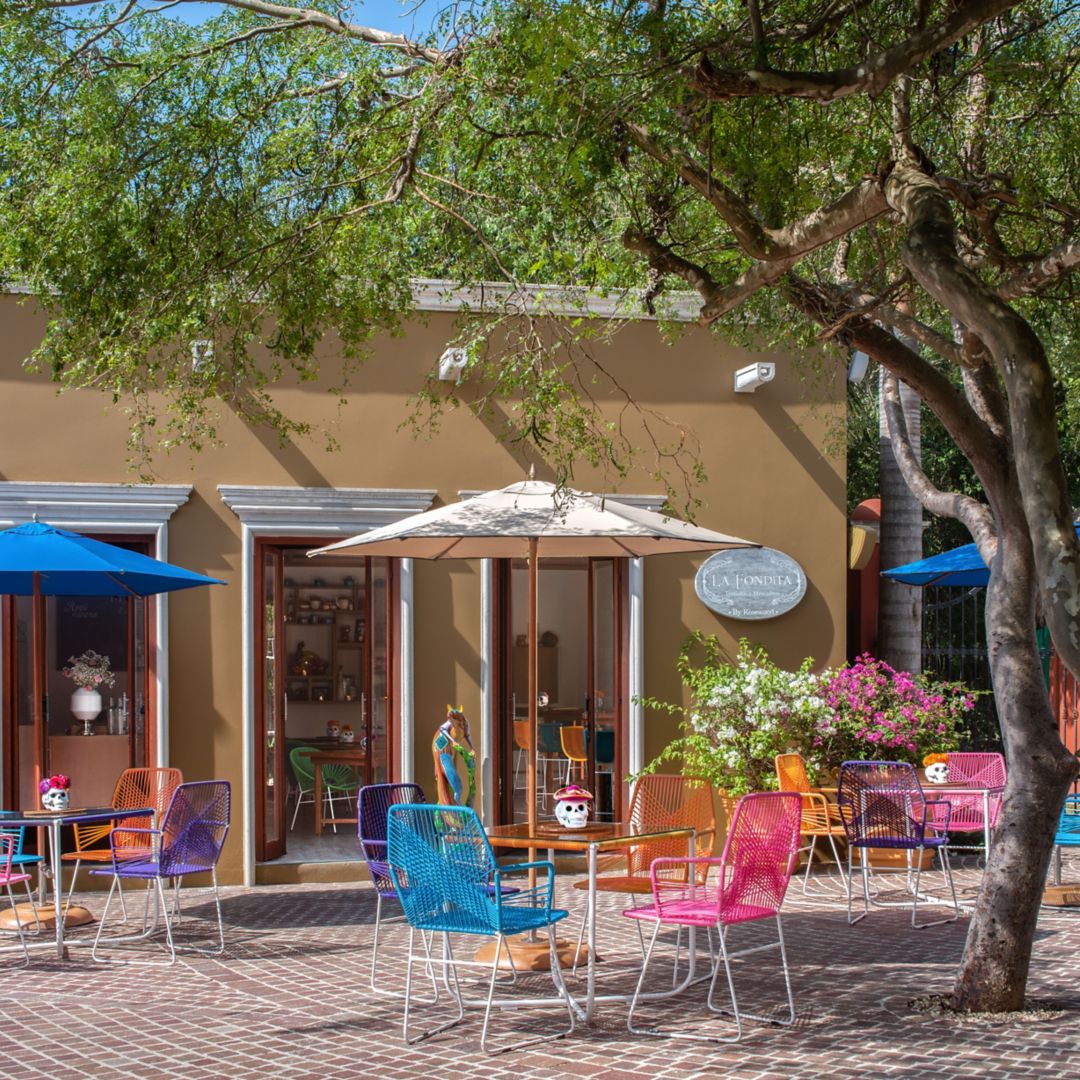 A vibrant outdoor café with colorful chairs and  tables under umbrellas.