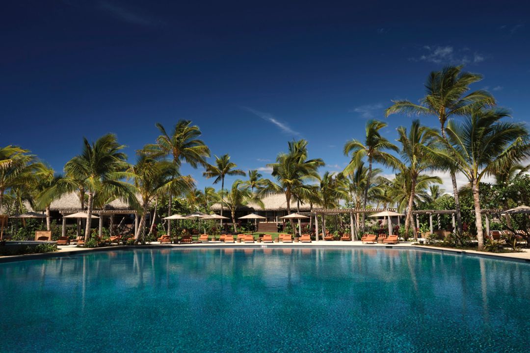 Luxury resort pool surrounded by palm trees and sun loungers under a clear blue sky.