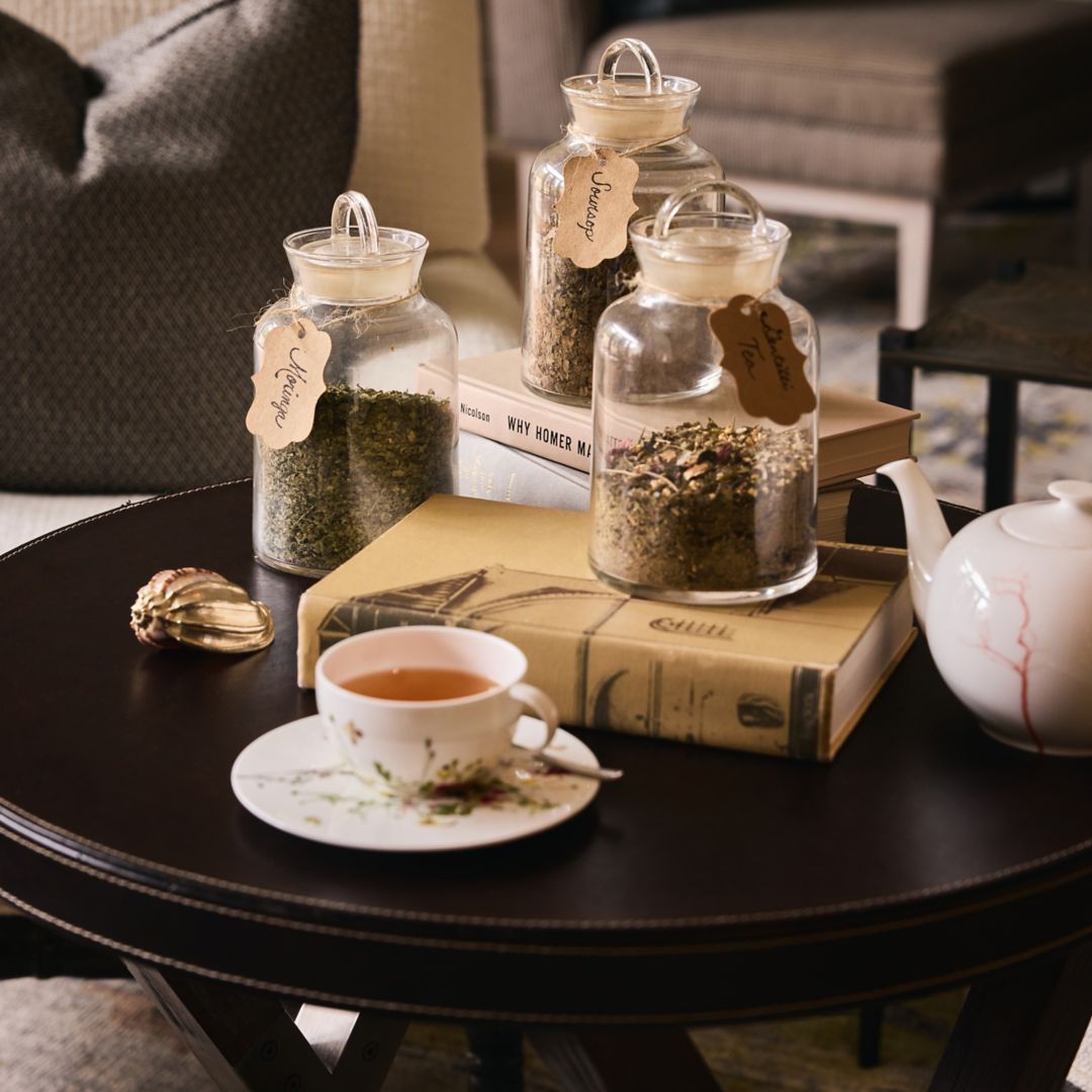 A table setting with a cup of tea, jars of herbs, a teapot, and books.