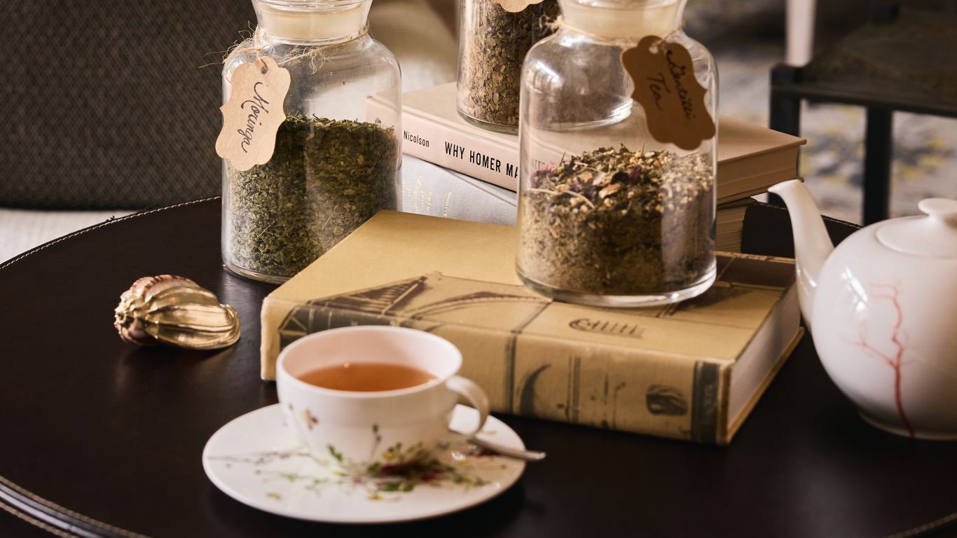 A table setting with a cup of tea, jars of herbs, a teapot, and books.