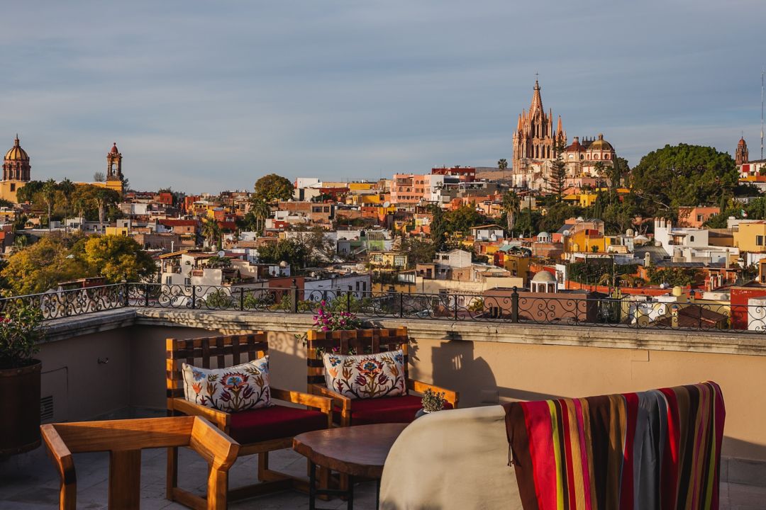 A rooftop bar in San Miguel with wooden furniture and colorful cushions overlooking a church in the background.