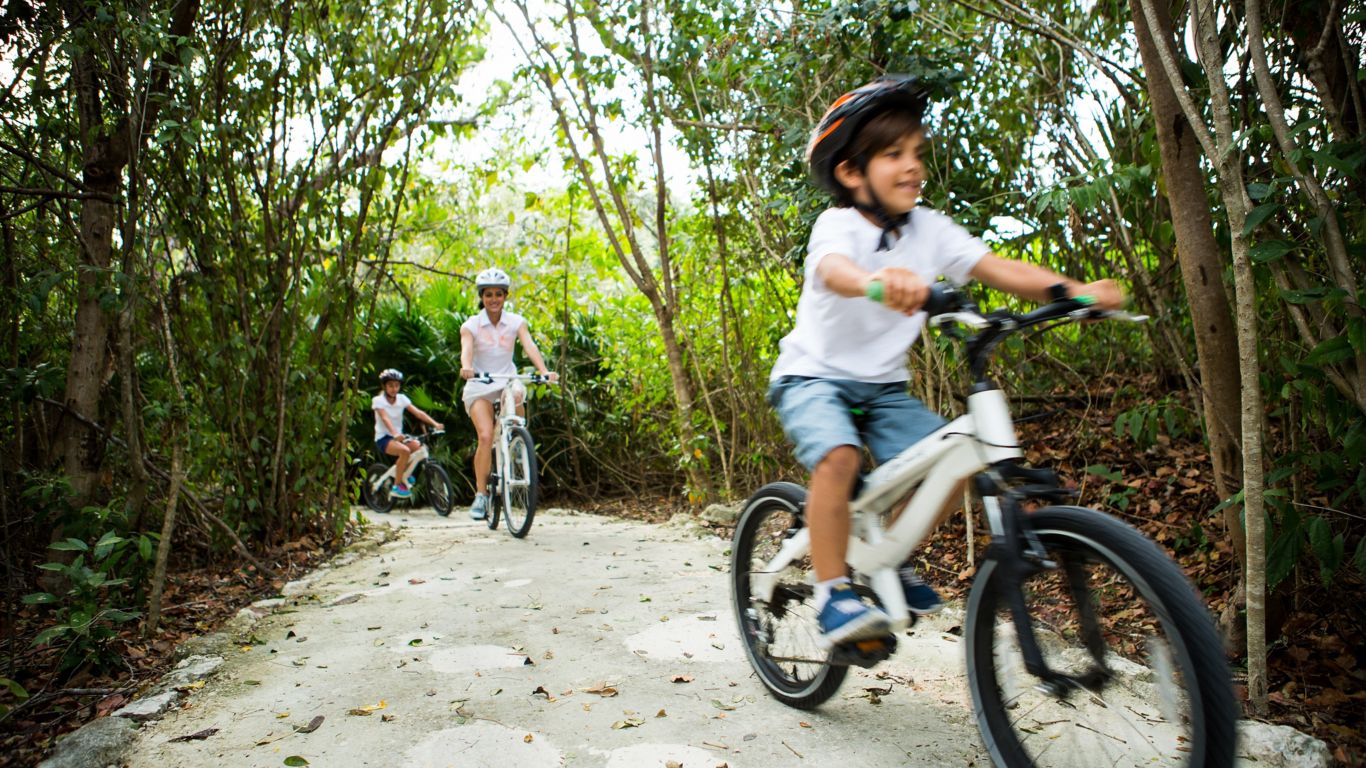 joven en su bicicleta con su madre y hermana en el sendero natural de Mayakoba