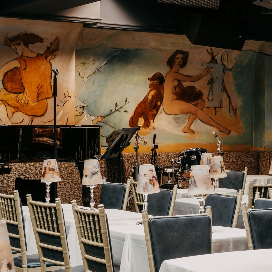 Dining setup with gold chairs and a mural of  figures and animals.