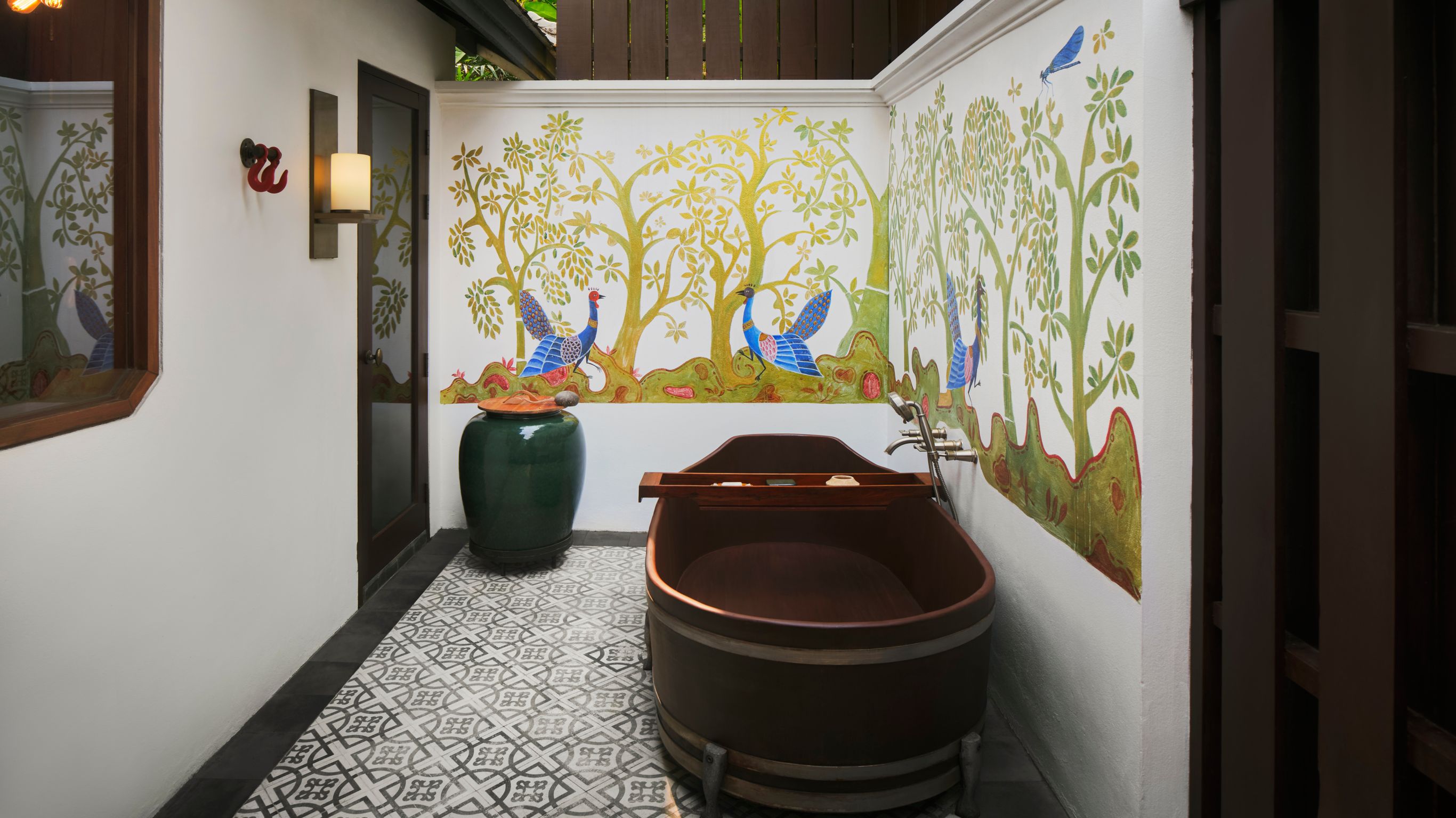A freestanding tub in an outdoor hotel room designed by Bill Bensley with decorated walls in Luang Prabang