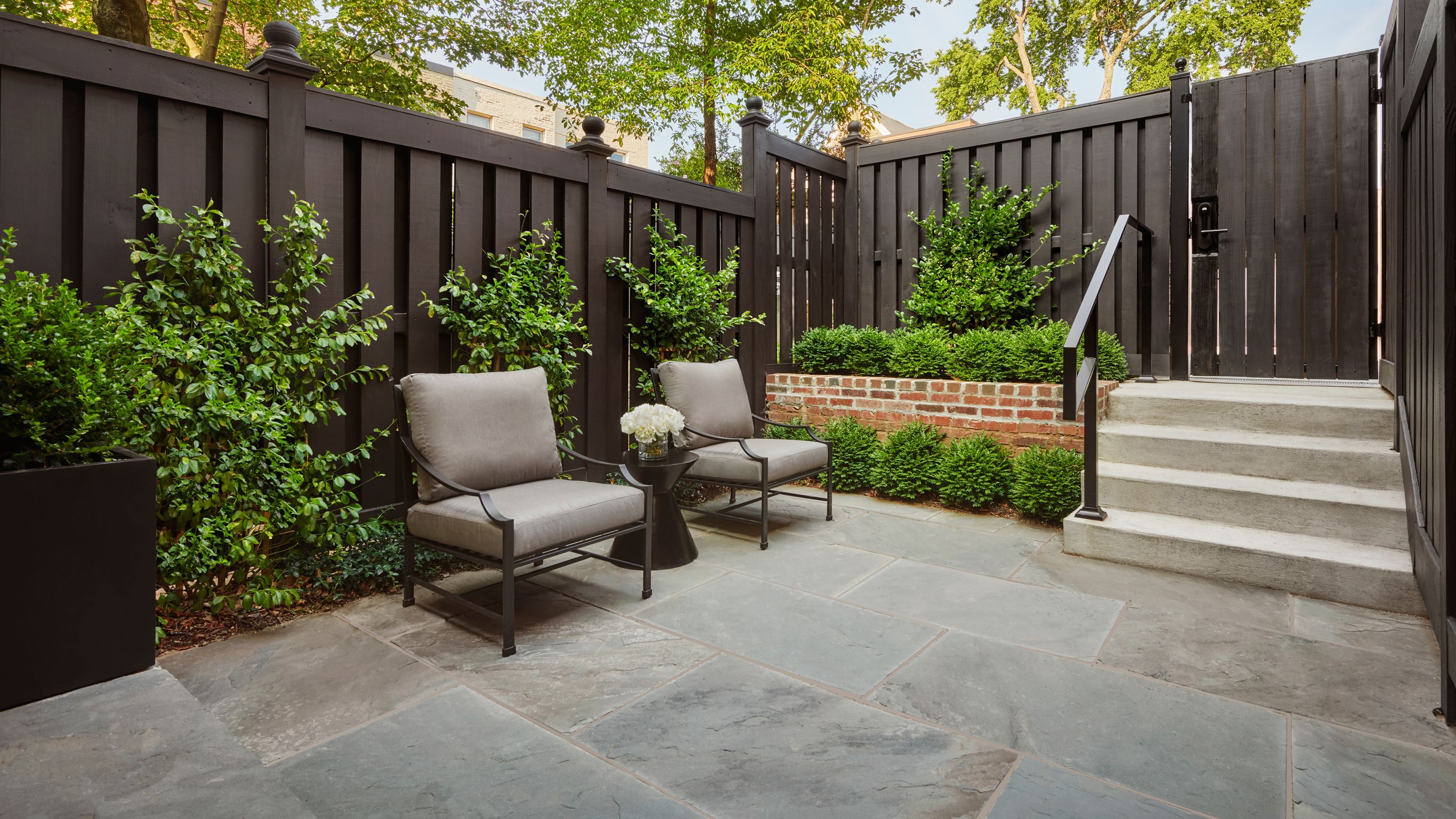 A townhouse patio with two chairs and a  small table with flowers.