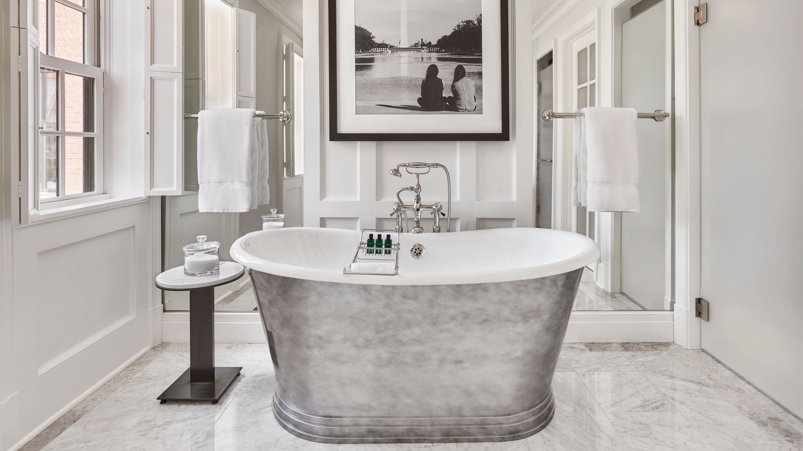 A bathroom with a freestanding bathtub, a  small table, and white towels.