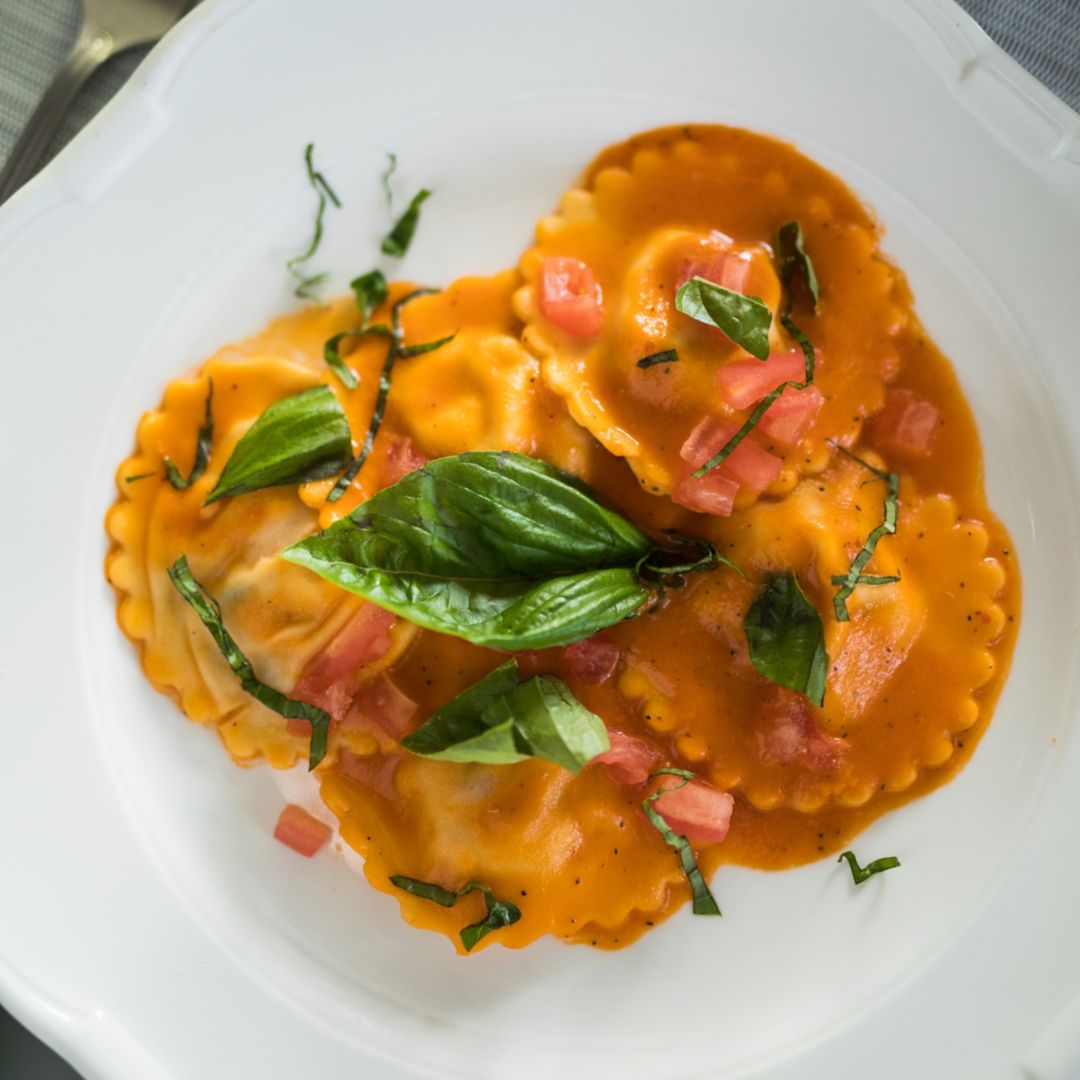 Ravioli all’aragosta topped with diced tomatoes and basil leaves on a white plate.