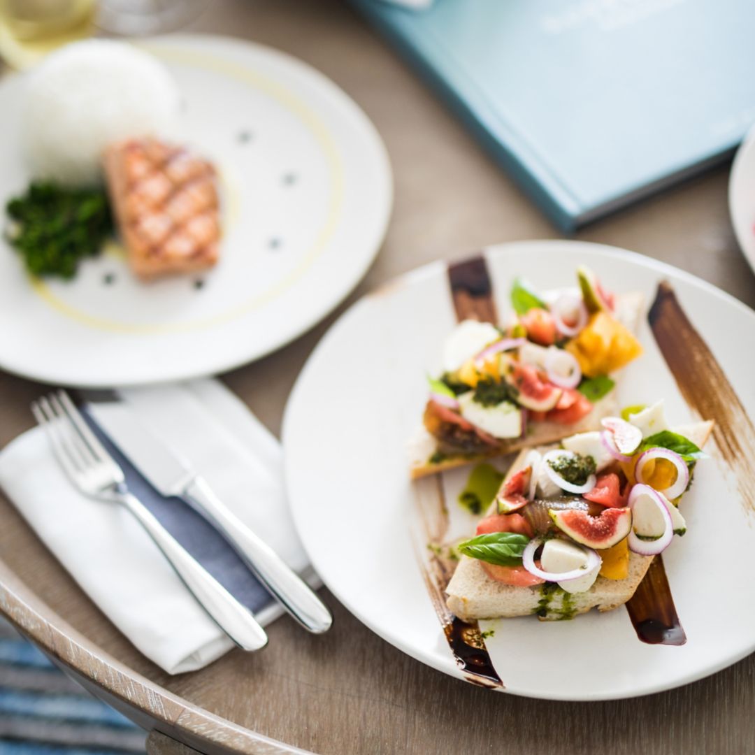 White plates are elegantly arranged with a beautifully prepared salmon dish and a plate of bruschetta..