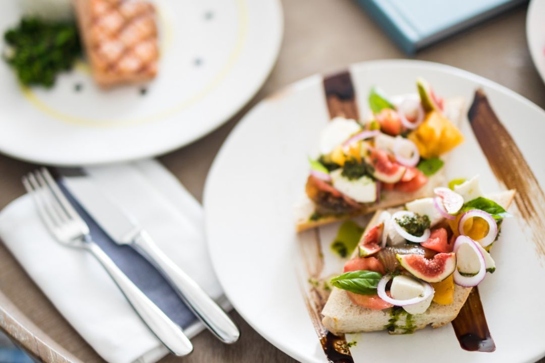 White plates are elegantly arranged with a beautifully prepared salmon dish and a plate of bruschetta..