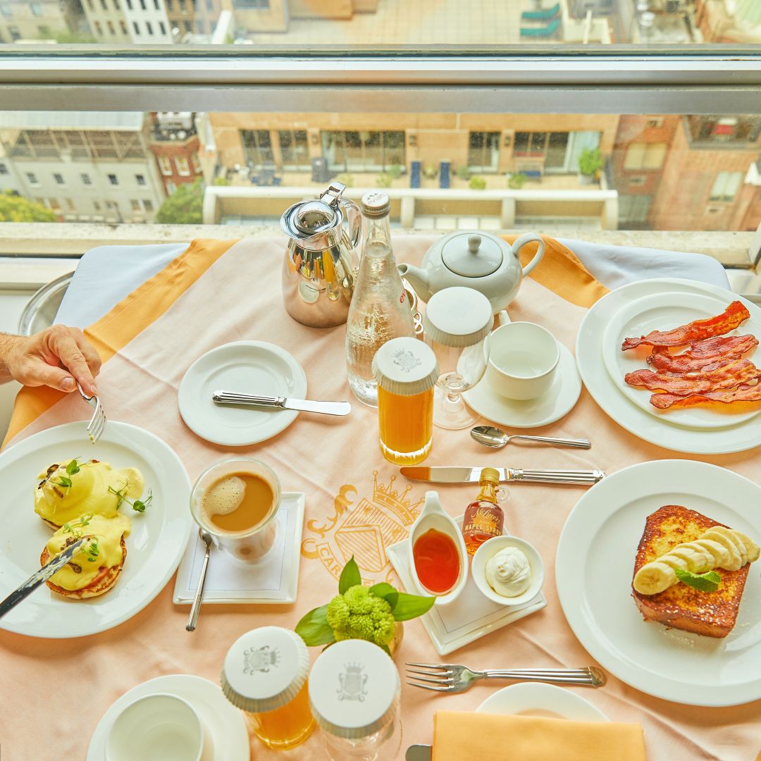Breakfast spread with eggs, bacon, toast,  coffee, and juice by a window.