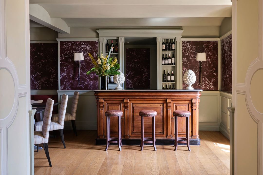 A bar area with a wooden counter, bar stools,  and a floral arrangement.
