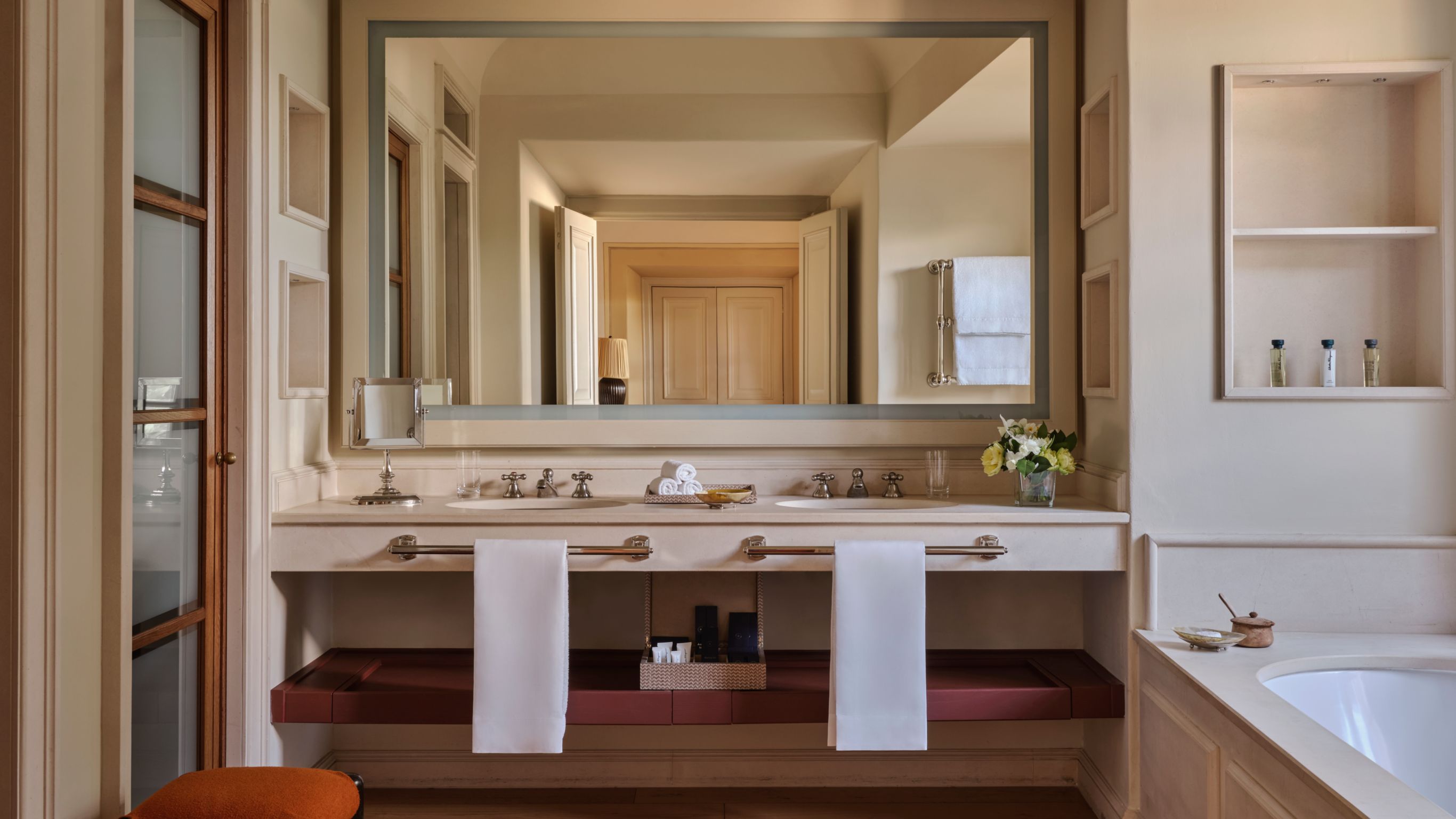 Double sink vanity with a large mirror, two white towels, toiletries, and a bathtub