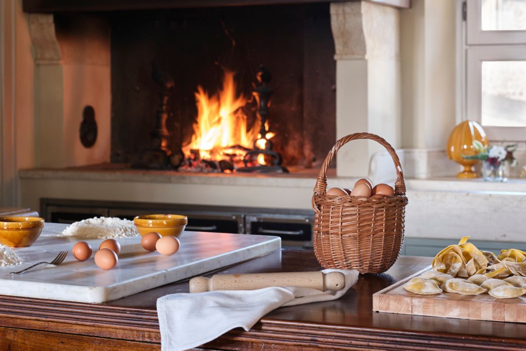 A wooden countertop with homemade pasta and eggs, set against a warm fire in the background
