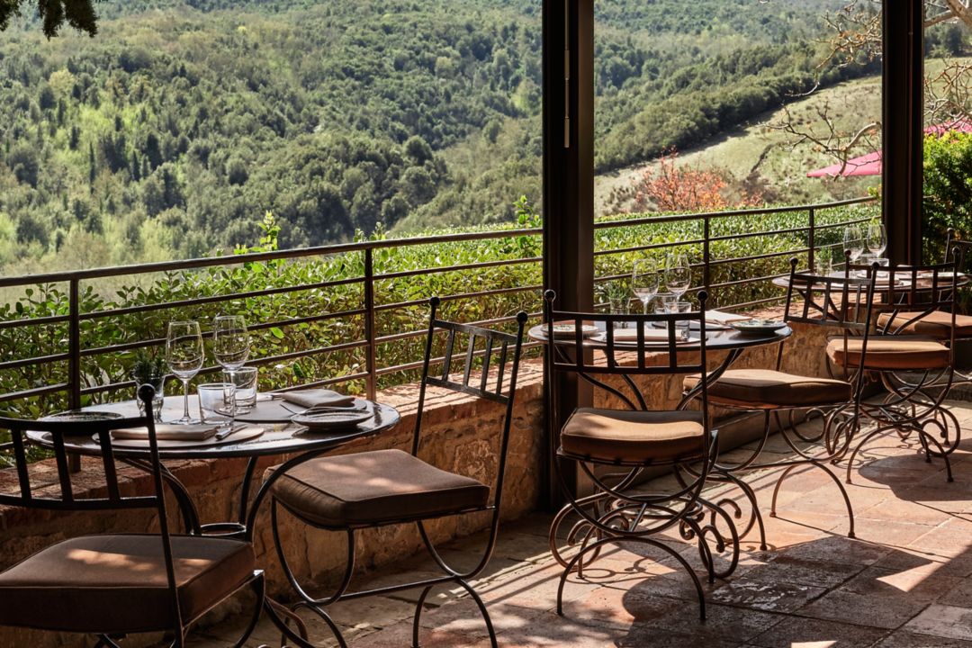 An outdoor restaurant terrace with small tables arranged with wine glasses and silverware