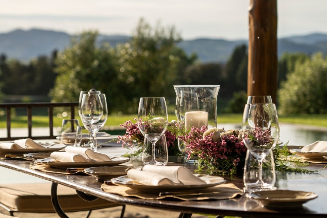 An outdoor dining table with folded napkins, wine glasses, and a floral centerpiece