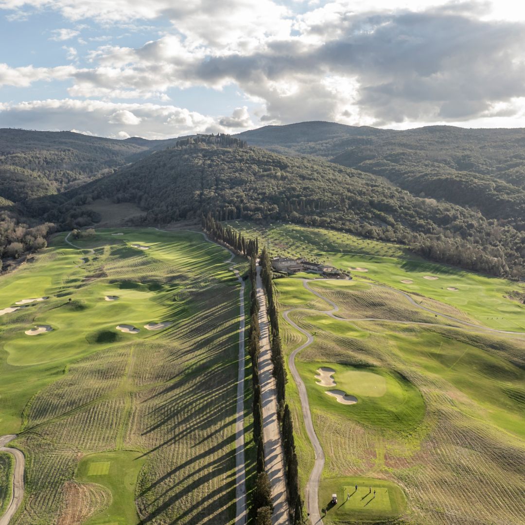 A golf course surrounded by mountains with a  long road in the middle.
