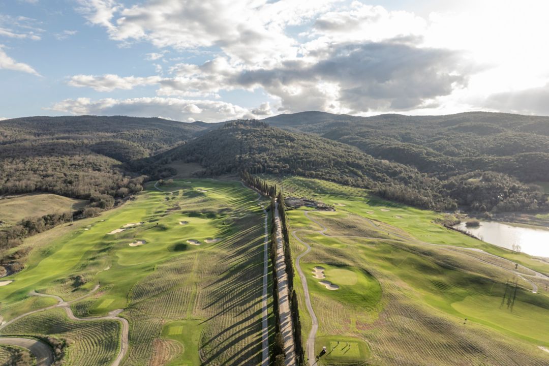 A golf course surrounded by mountains with a  long road in the middle.