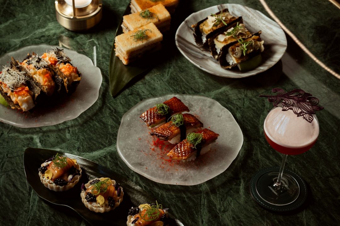 A variety of dishes and a red cocktail displayed on a green marble table.