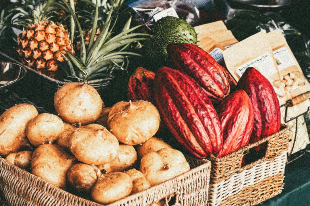 Baskets filled with potatoes, cocoa pods, and a pineapple, showcasing a variety of fresh produce.