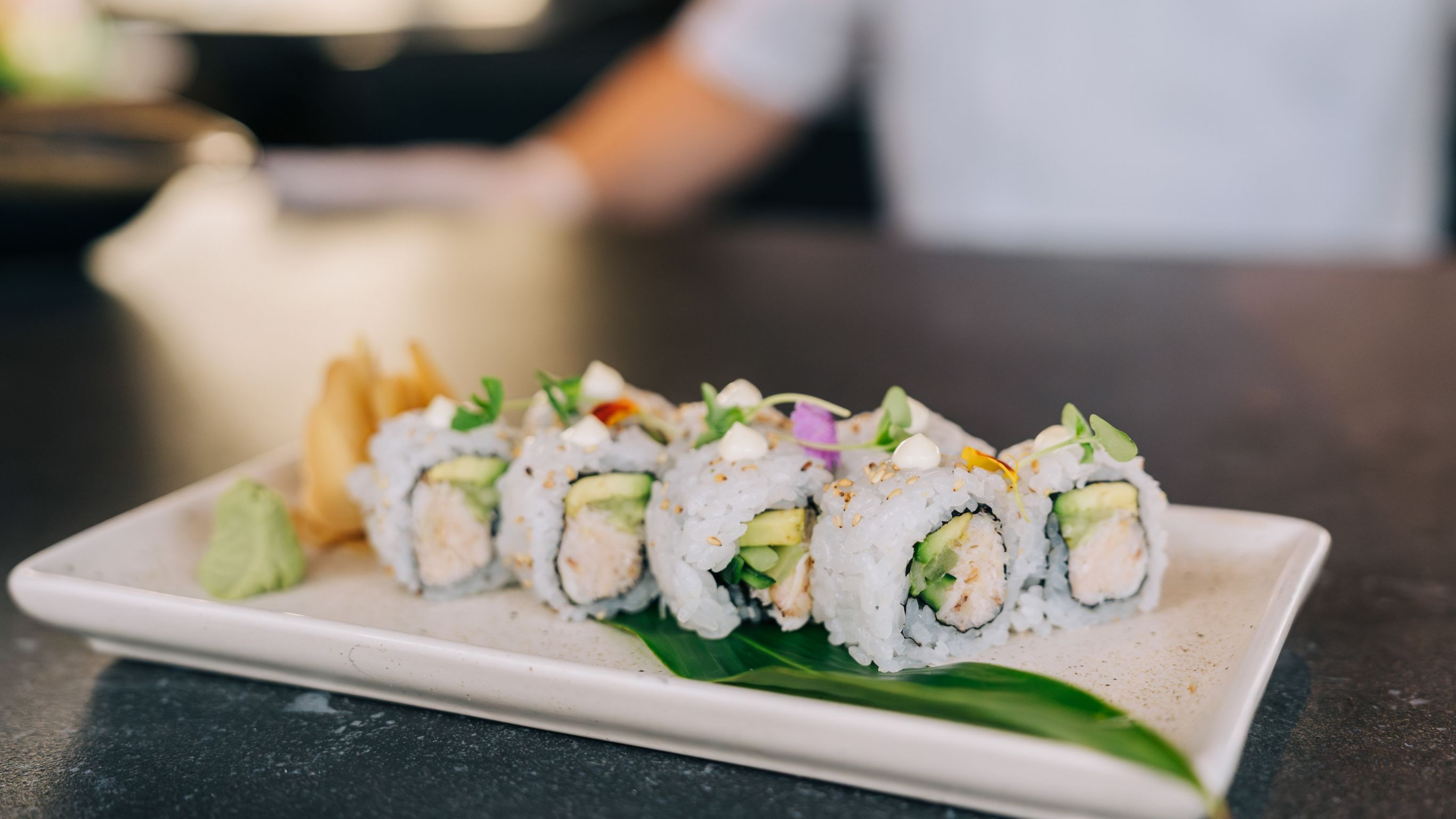 A white plate with sushi rolls topped with microgreens and sesame seeds.