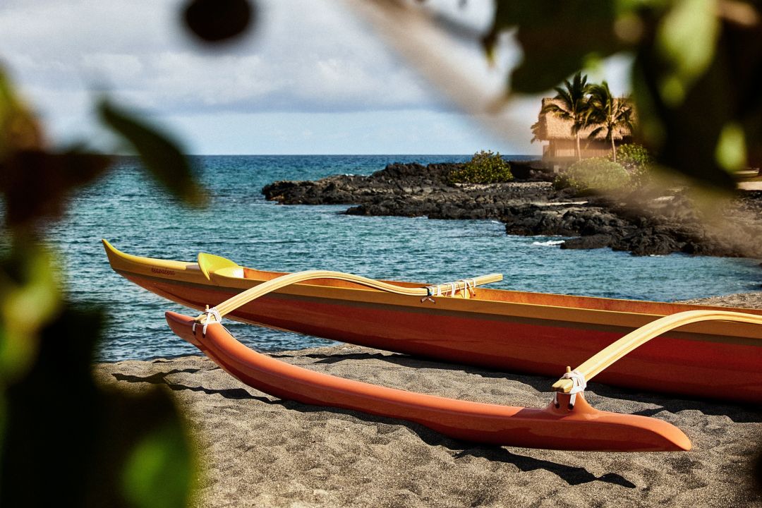 A canoe resting on a beach in Hawaii with the  ocean in the background.
