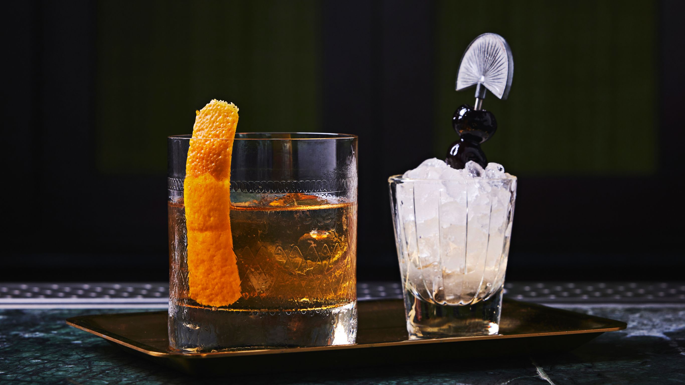 Two glasses on a tray: one with an orange peel, the other with ice.