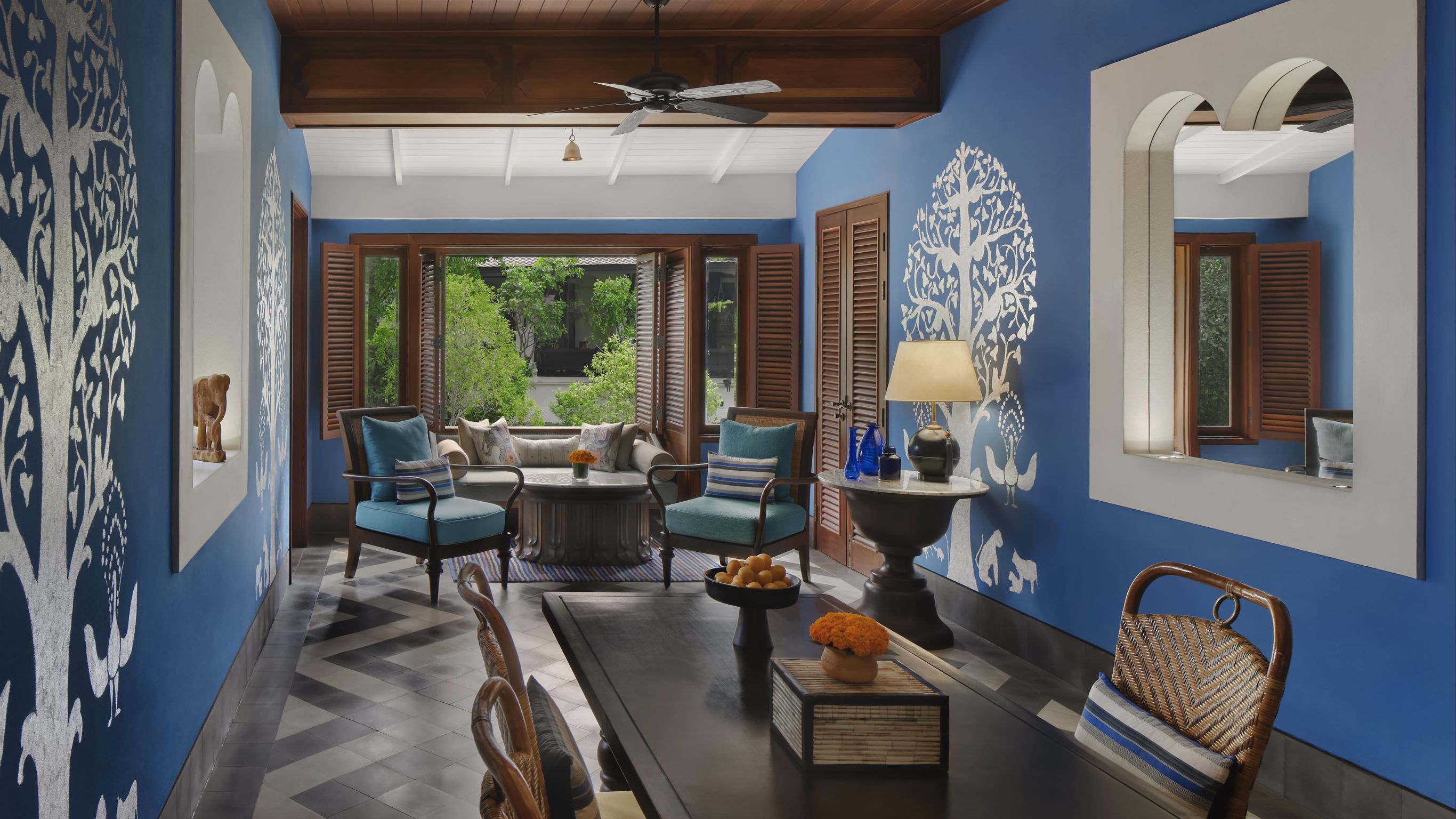 Bill Bensley designed hotel suite living room with blue walls, wooden ceiling, and decorative wall art, featuring a seating area and large windows, in Luang Prabang