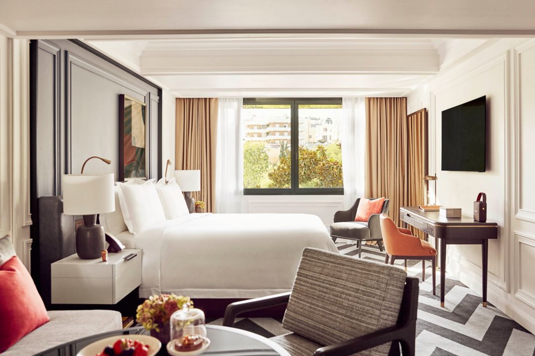 interior of the Junior Suite Castellana bedroom showing a king bed with white sheets across from a wall mounted television at the Villa Magna luxury hotel in Madrid