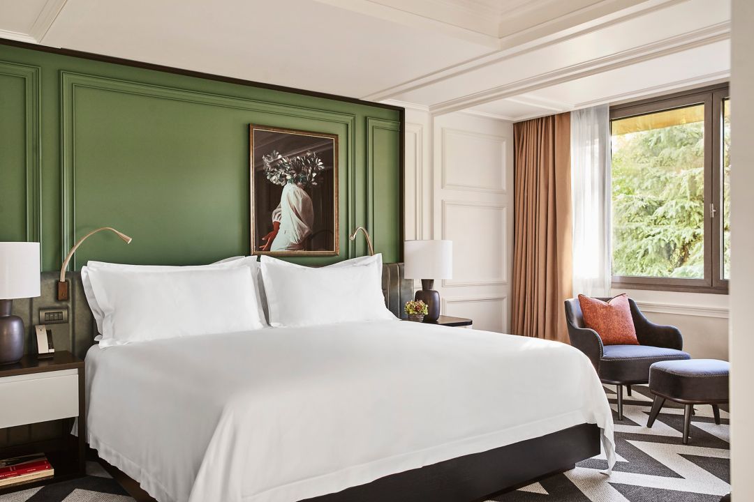 Interior of the Villa Magna Suite bedroom showing a king bed with white sheets and green painted walls at a luxury hotel in Madrid