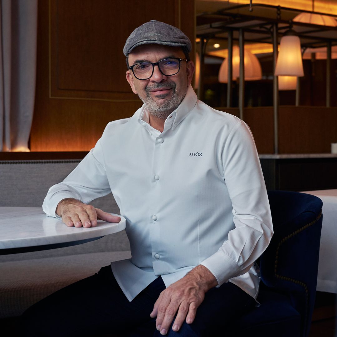Jesús Sánchez dressed in a white chef's jacket, sitting at a table in a restaurant setting