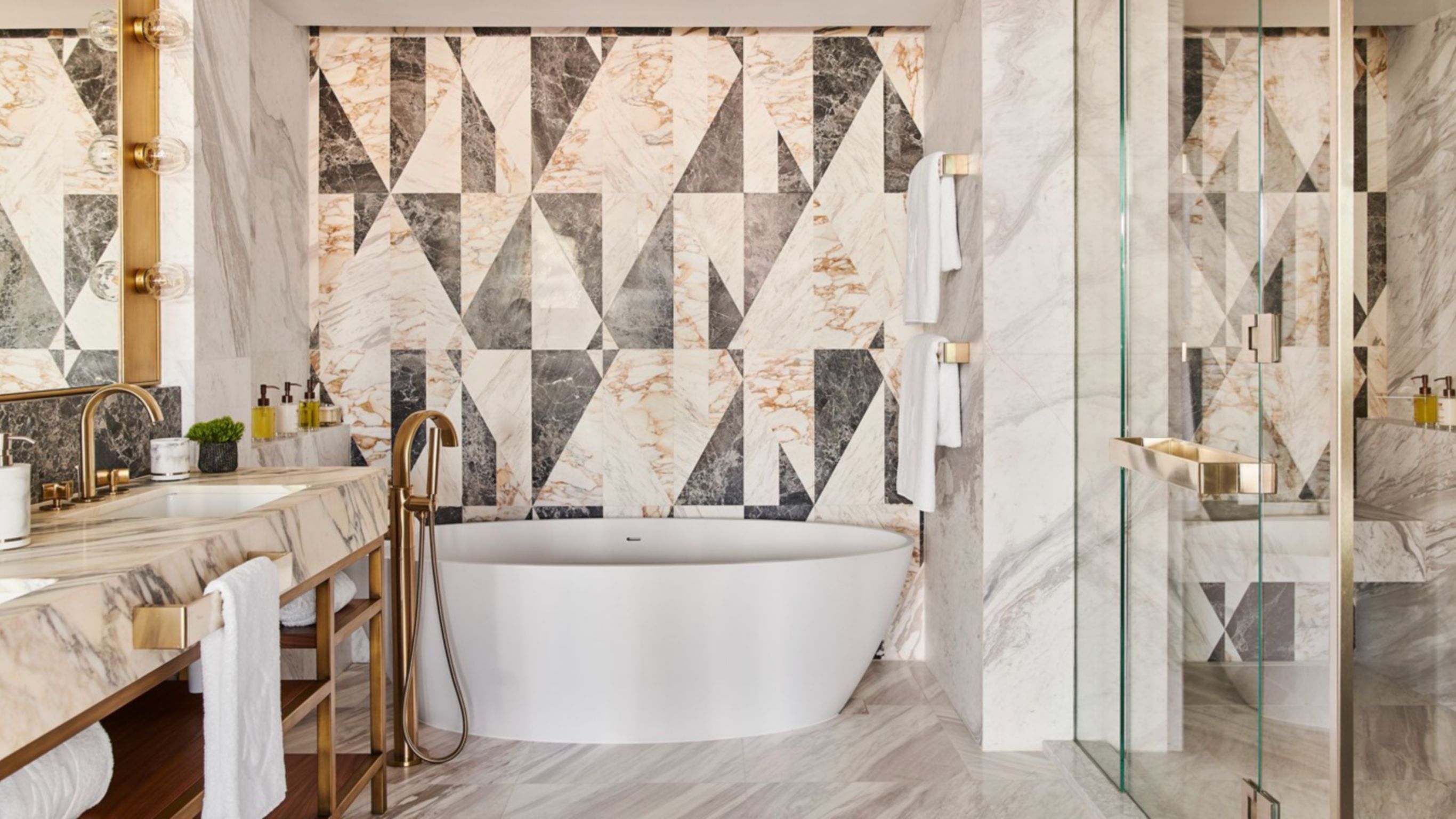 A luxury hotel bathroom with a full-sized bathtub next to marble walls, and two sinks in front of a mirror
