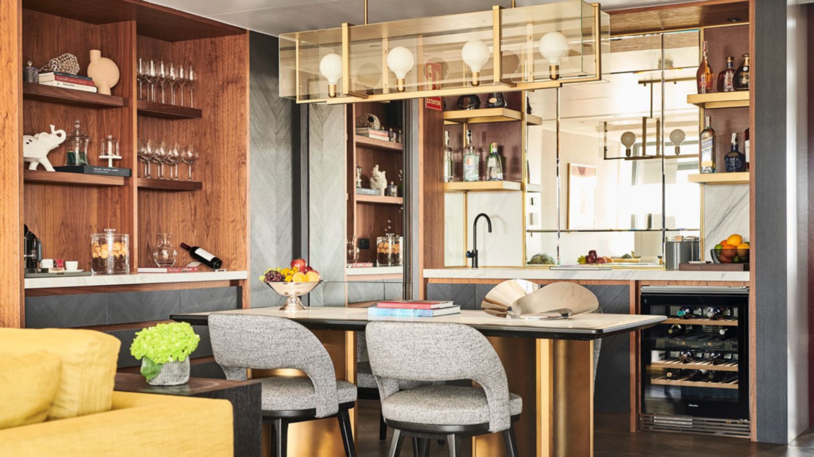 A modern hotel bar with bar stools, decorative shelves along the walls, and liquor bottles in the background.