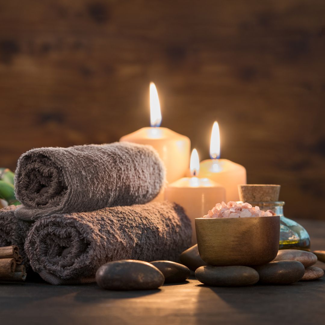 A relaxing spa setup with rolled towels, candles, himalayan salt, and smooth stones.