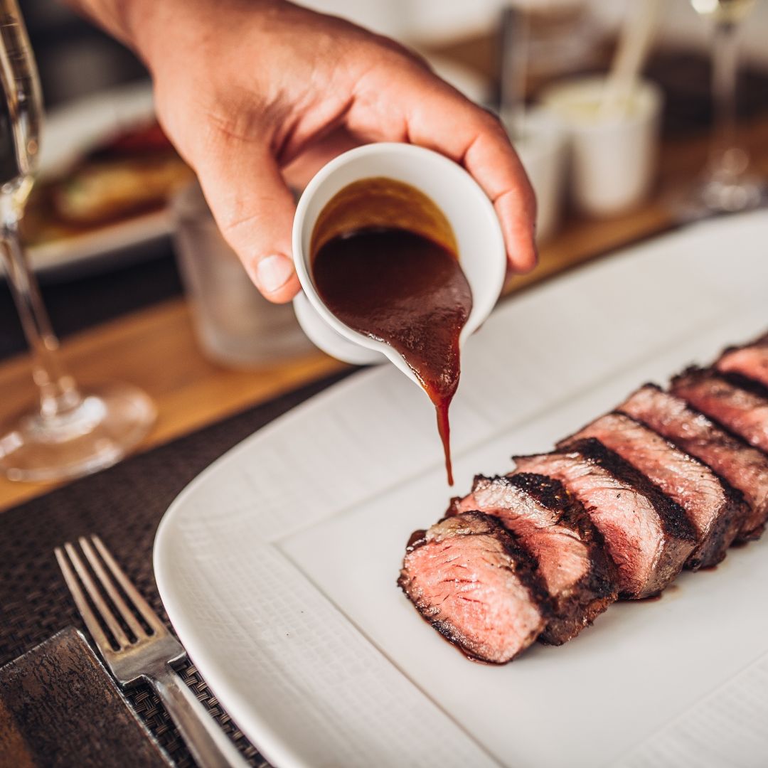 A waiter pours sauce on a plate of sliced  steak.
