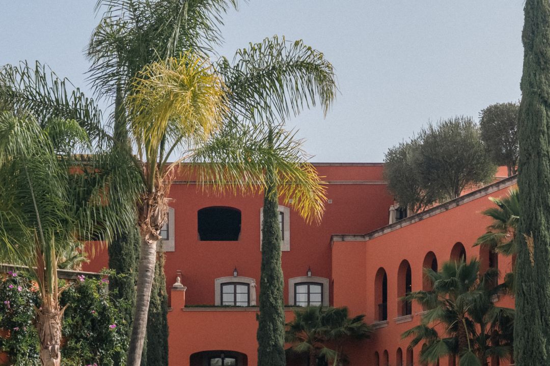 Área de alberca de hotel con camastros bajo toldos, palmeras y toallas enrolladas.