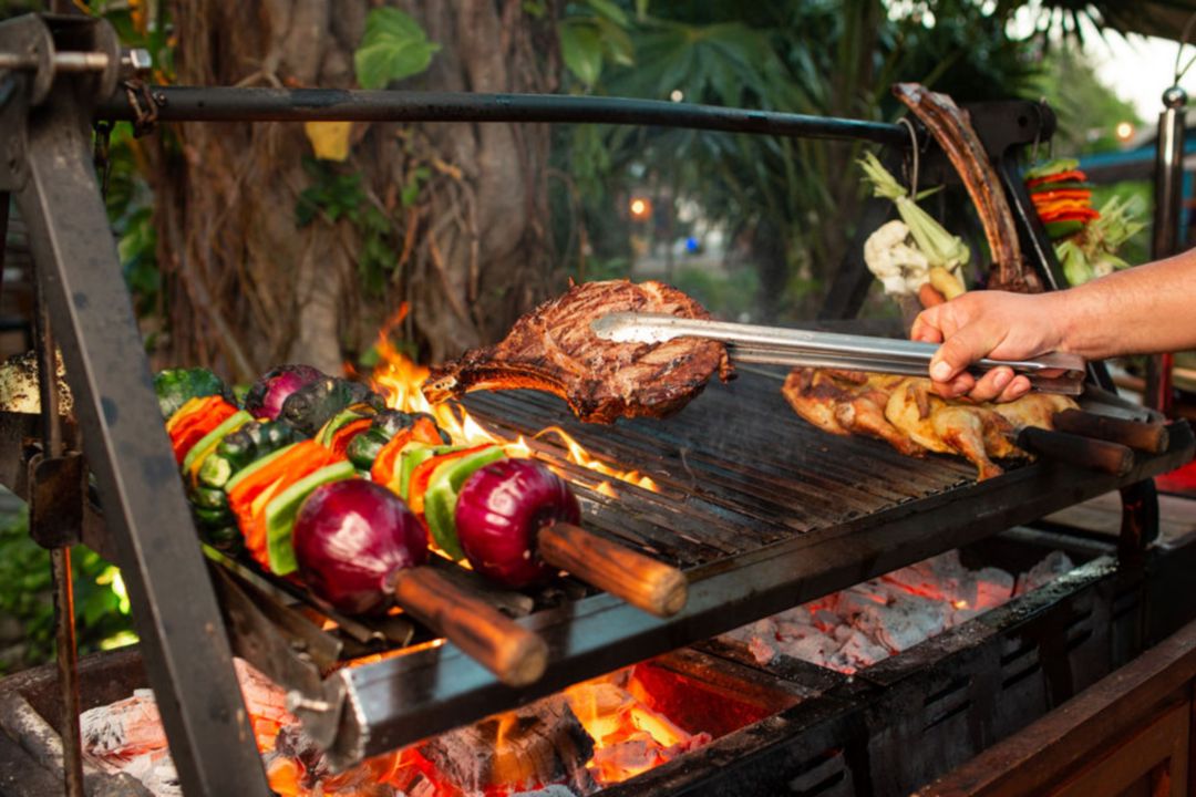 Meat and vegeatables cooking over an open flame grill