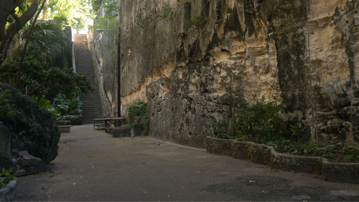 A stone pathway with benches and a staircase leading up a rocky cliff.